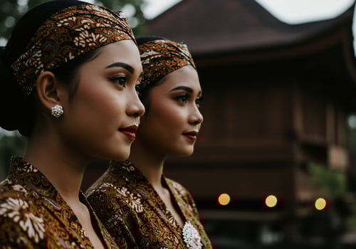 Two traditionally dressed women in profile near a Javanese house, cultural event photo