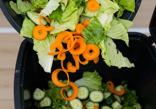Vegetable food waste dropping to trash bin for recycling in a modern kitchen photo