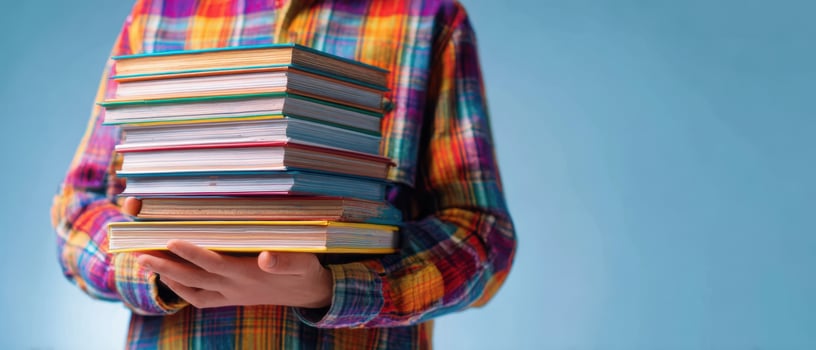 The child holding a colorful stack of books against a blue background. photo
