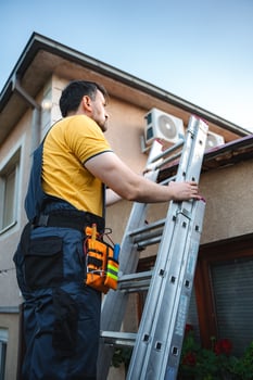 Technician climbing a ladder and installing an air conditioner on a building facade photo