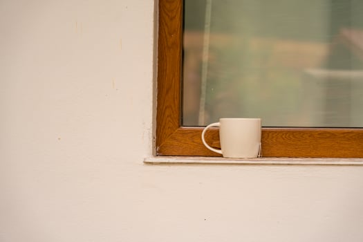A white mug of tea or coffee rests on a wooden windowsill of a countryside home photo
