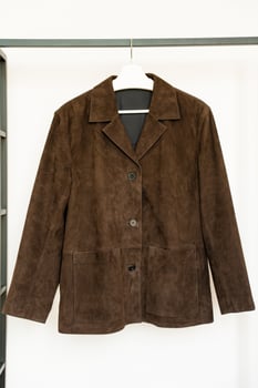Dark brown suede jacket with buttons and patch pockets hanging on white hanger in bright room photo