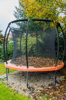 Trampoline in backyard covered with autumn leaves surrounded by colorful trees and garden greenery photo