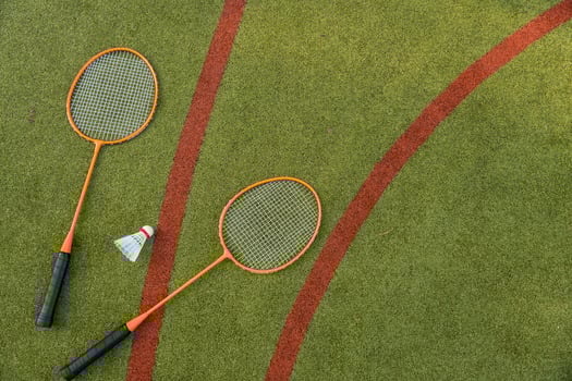 Two orange badminton rackets and a shuttlecock rest on a green sports field, captured from above. photo