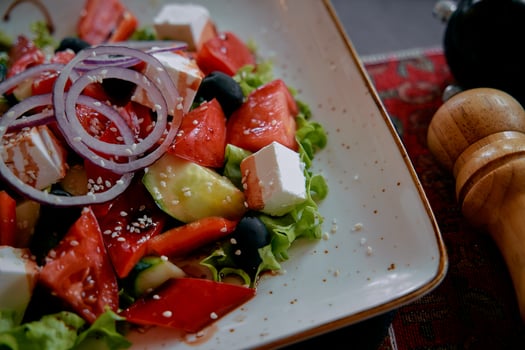 A Colorful Salad Featuring Fresh Vegetables, Feta Cheese, Olives, and Topped with Red Onions Served in an Elegant Bowl photo
