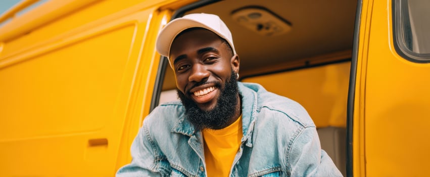 The cheerful man smiling by a vibrant yellow van in a sunny outdoor setting. photo