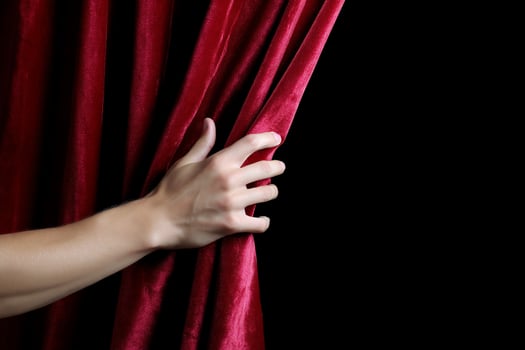 A hand pulls back a luxurious, draped red velvet curtain on a black background photo