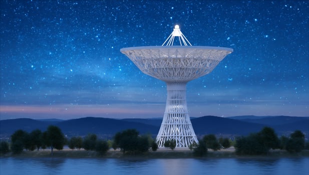 A large radio telescope illuminates the night sky over a body of water photo