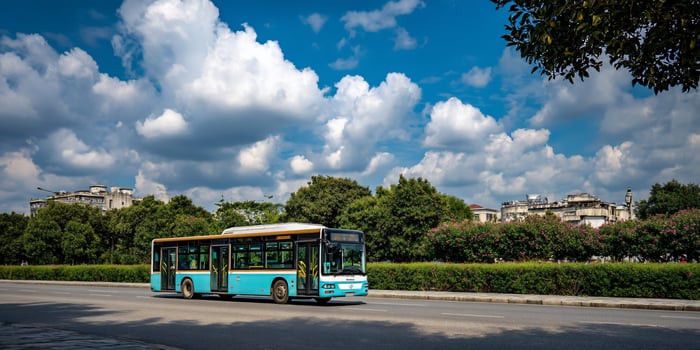 Blue bus travels on a city street under a sky full of fluffy white clouds photo