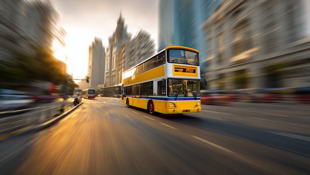 Double-decker bus speeding on city street with sunlight reflecting off the asphalt photo