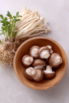 Enoki and cremini mushrooms, with roots, in bowl on bright neutral backdrop photo