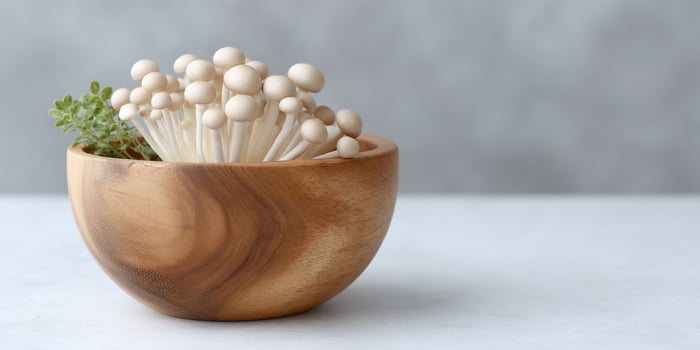 Fresh enoki mushrooms and herbs nestled in a rustic wooden bowl on a white surface photo