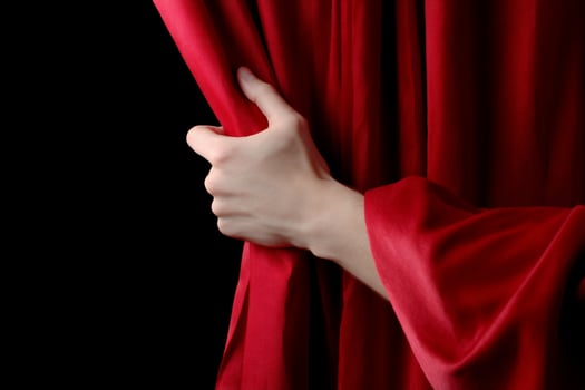 Hand parts red fabric in front of black background, dramatic, artistic, bold photo