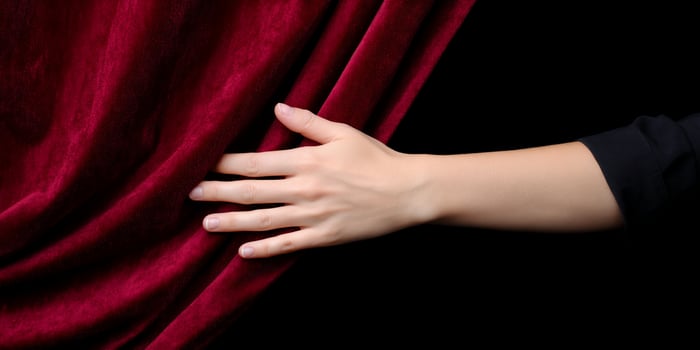 Hand pulls deep red velvet curtain against the dark, revealing something more photo