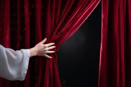 Hand pulls back a rich red curtain revealing a dark space with a subtle spotlight photo