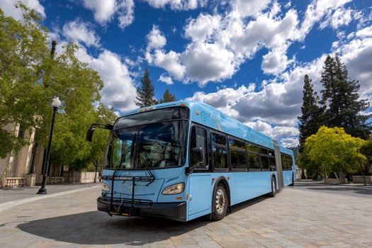 Light blue bus on a gray brick road with building backdrop and a cloudy sky photo