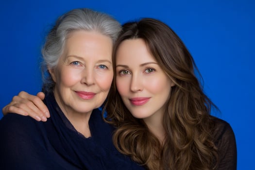 Older and younger women smile, embracing with grace in front of a blue backdrop photo