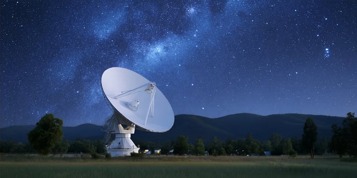Radio telescope on grassy field under dark night sky with stars and galaxy photo