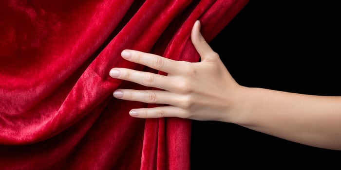 Red velvet curtain being pulled back, revealing a dark black background photo