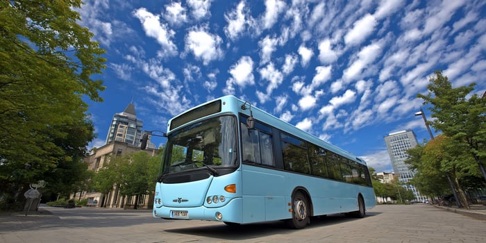 Skyward bus on sunny day with trees and buildings under wispy cloud formations photo