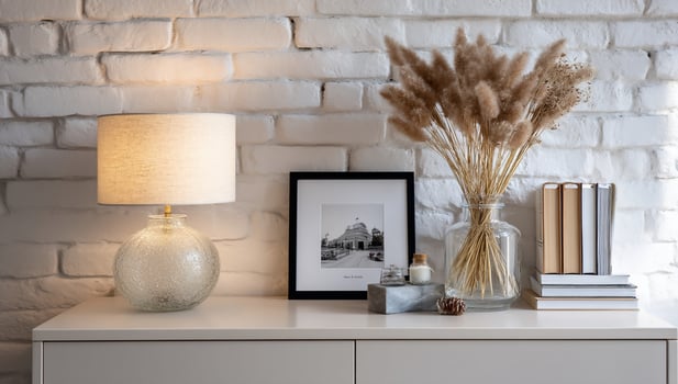 Table still life featuring dry plants, picture frame, lamp and books on a dresser photo
