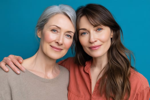 Two smiling women with rosy cheeks and natural skin are posing on blue background photo
