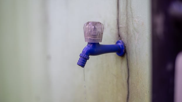 Close-up of a blue plastic faucet dripping water, mounted on a stained wall. photo