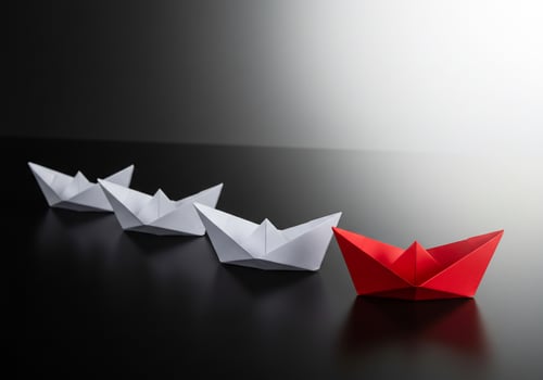 A red paper boat is in the middle of a row of white paper boats photo