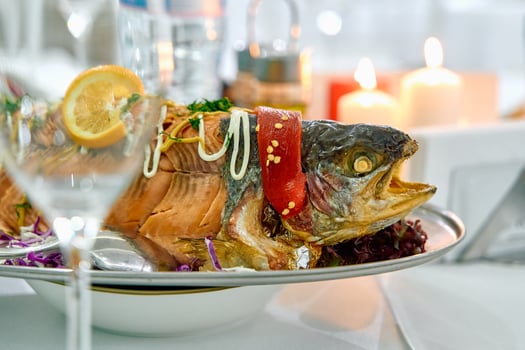 A beautifully presented roasted fish dish garnished with lemon and colorful vegetables, set elegantly on a dining table surrounded by soft candlelight. photo