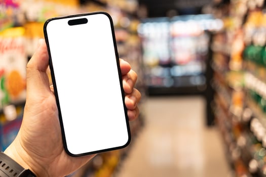 Hand Holding Smartphone with Blank Screen in Supermarket. a blank white screen. The background is a blurred supermarket aisle. shopping, mobile commerce, online shopping concepts. Copy Space. photo