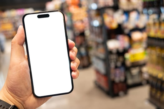 Hand Holding Smartphone with Blank Screen in Supermarket. a blank white screen. The background is a blurred supermarket aisle. shopping, mobile commerce, online shopping concepts. photo
