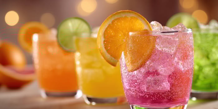 Colorful cocktails lined up on bar, fruit garnishes, lights in background photo