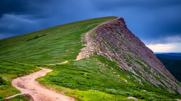 Dramatic mountain trail winds up a rocky summit under moody skies. photo
