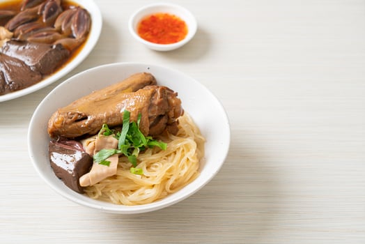 dried noodles with braised duck in white bowl on wooden background photo