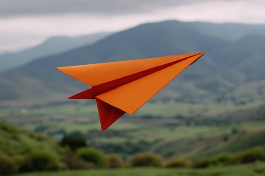 Orange paper airplane soaring, flight over nature landscape, hills background photo