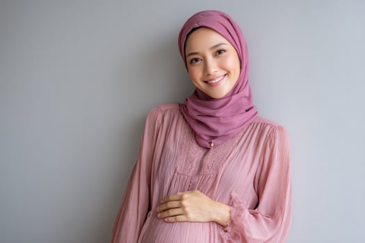 Pregnant woman in hijab smiles against grey wall, maternal wellness lifestyle image photo
