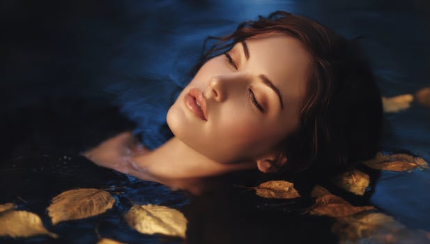 Woman floating peacefully on dark water surface among autumn leaves, relaxing photo