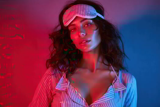 Woman wearing a sleep mask, pajamas, indoors, illuminated by red and blue light photo