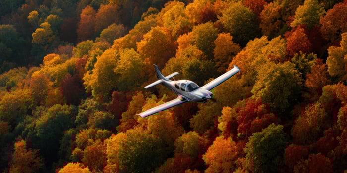 A light aircraft flying over a forest of autumn colored leaves and trees below it photo
