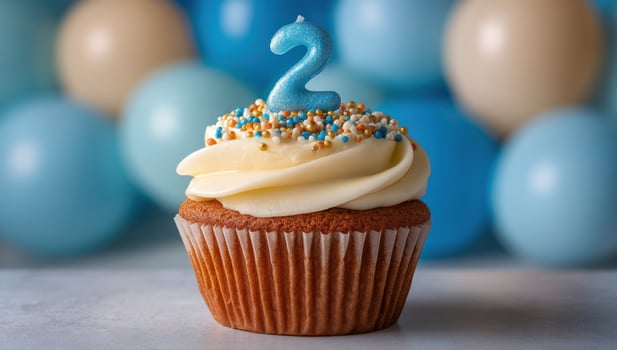 A frosted cupcake with a number '2' candle against balloon background photo