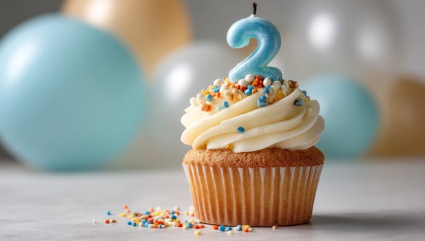 Cupcake with two candles on top of a table with balloons photo
