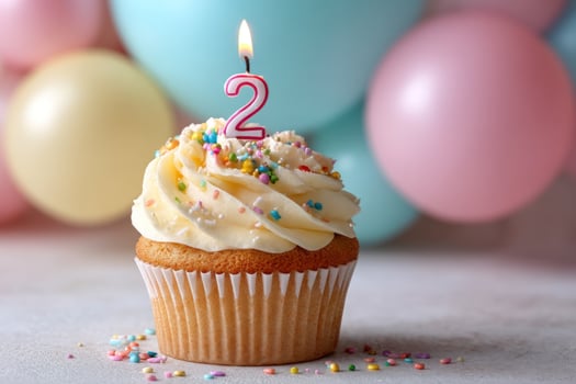 Cupcake with candle '2' and sprinkles, balloons blurred in background, party time photo