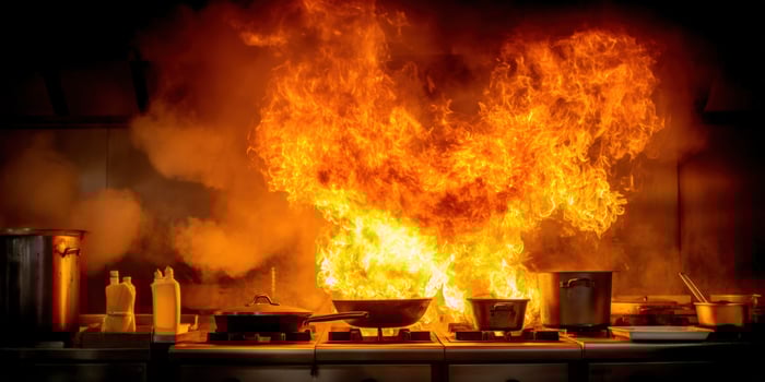Flames engulf pots and pans on a gas stove in a kitchen with smoke rising photo