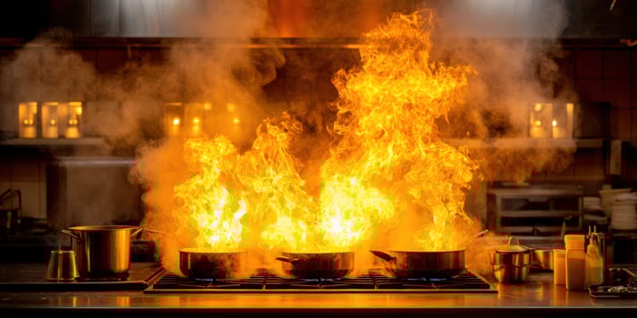 Flames erupt over cooking pots on a stainless steel stove top and in a kitchen photo