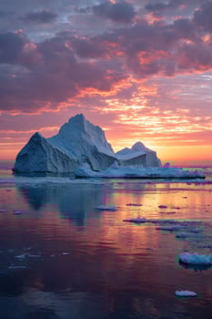 Iceberg floats on water under colorful sunset, reflecting in its surface photo