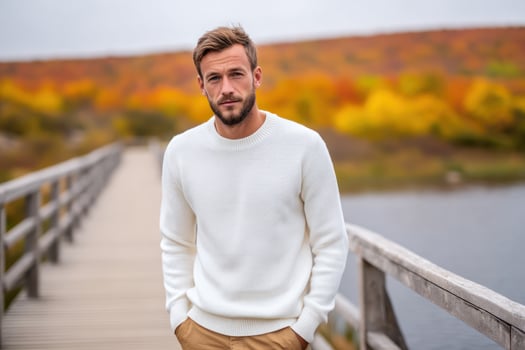 Man poses on wooden bridge, autumn leaves and lake as a backdrop, peaceful photo