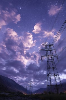 Power lines cross a valley at night with stars and clouds. Energy infrastructure photo