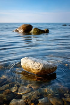 Rock rests in calm water, rings expanding, serene backdrop of ocean and sky photo