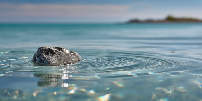 Rock in clear water with ripples, reflecting sunlight with island background photo