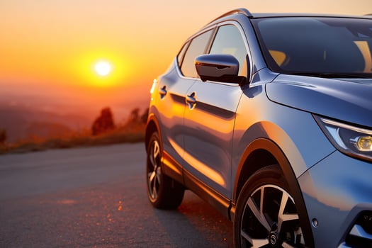 Blue crossover on road at sunset with orange sky, mountains in background photo